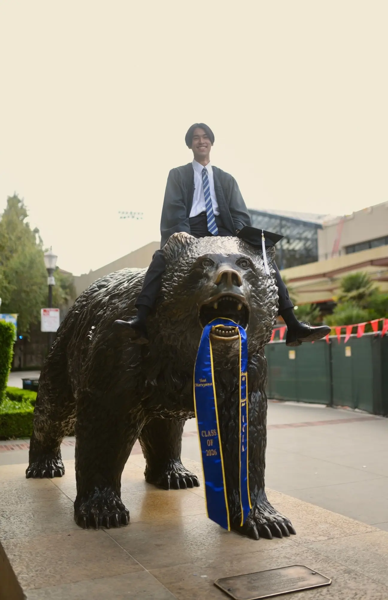 卒業式のガウンを着て、UCLAのブルーインベア像に座る丸山勇依